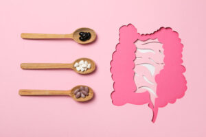 The photo shows three spoons with different pills beside a pink paper cutout of the digestive system, linking supplements to gut health.