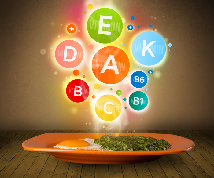 A plate with eggs and greens topped with colorful floating vitamin icons (A, B, C, D, E, K), symbolizing the nutritional value and health benefits of whole foods