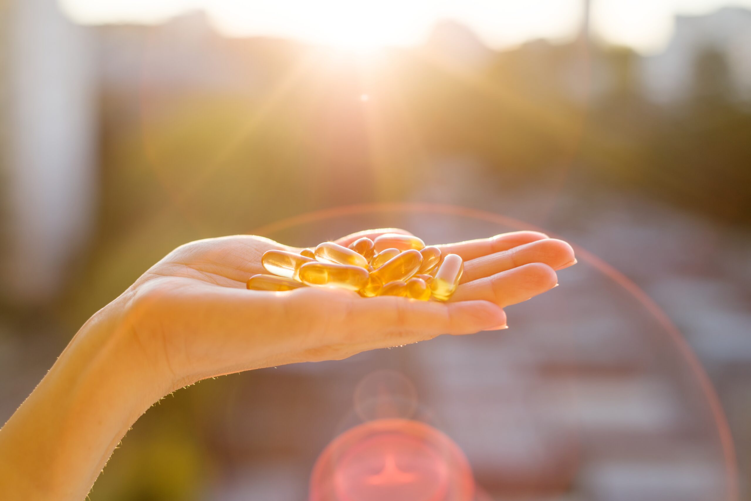Hand of a woman holding fish oil Omega-3 capsules, urban sunset background.