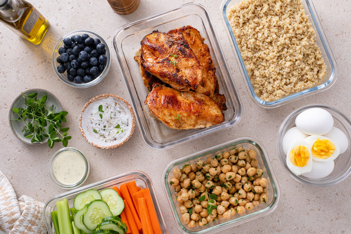 High protein healthy lunch meal prep in containers with chicken, quinoa, herbed chickpeas, vegetables and boiled eggs.