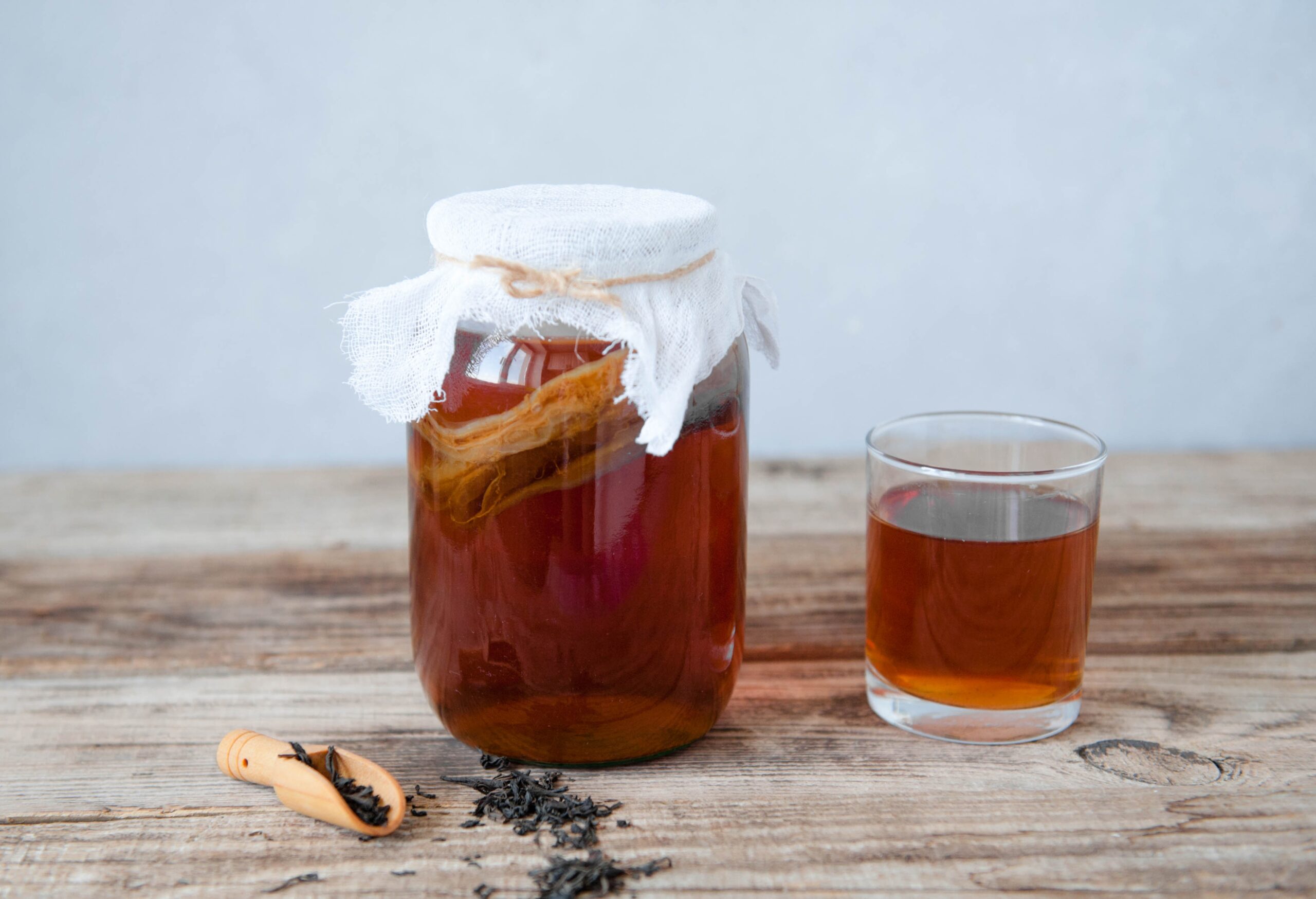 Homemade fermented kombucha tea in a glass jar and in a glass cup on a wooden and gray background.
