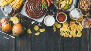 Beer and snack set. Variety of beers, grilled sausages, burgers, corn, fried potatoes, chips, salted almonds and sauces on dark wooden background.